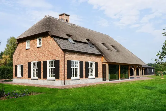 Foto van een woonboerderij met een rieten kap met een metselwerk gevel. De ramen bestaan uit ruitjes met traditionele luiken. Aan de achterkant zit een aanbouw.